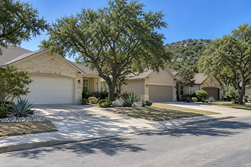 Closed garage doors face a quiet street lined with stone homes and trees.