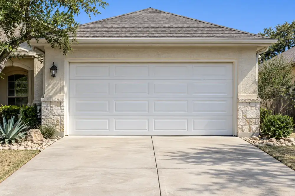 Closed, level white garage door on a stucco house with an empty driveway
