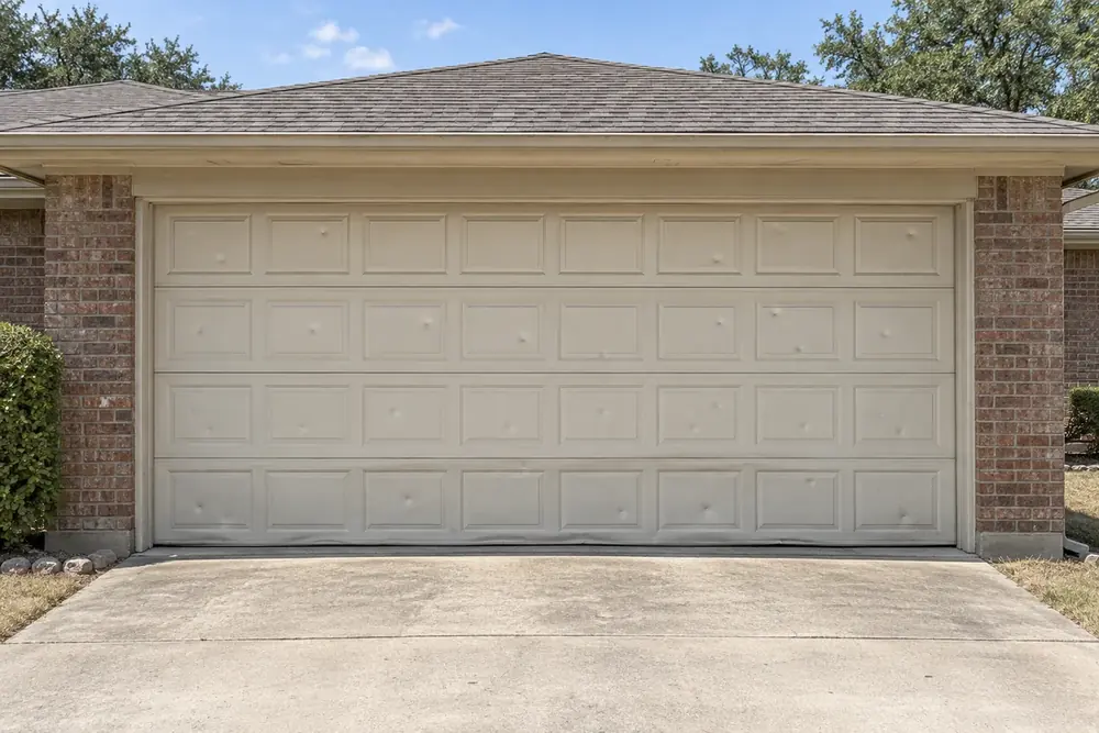 Faded almond garage door with scattered dents and a bowed bottom section