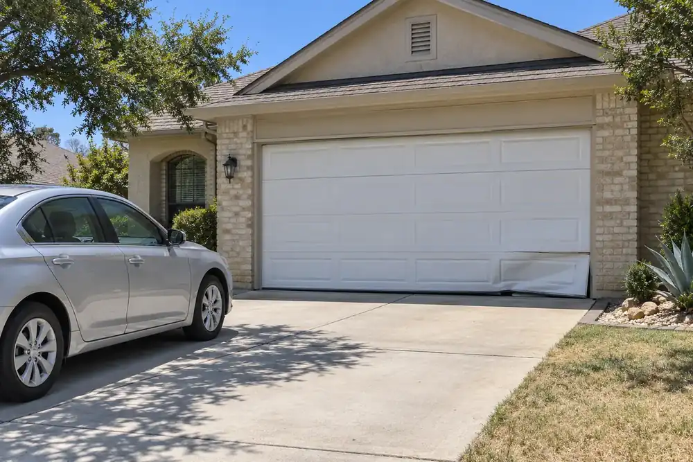 Crooked white garage door with a creased bottom corner beside a silver sedan