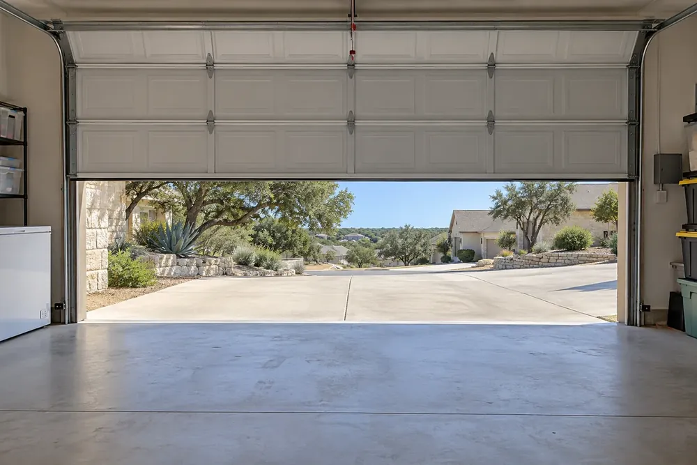 Level white sectional garage door halfway open above a swept garage floor