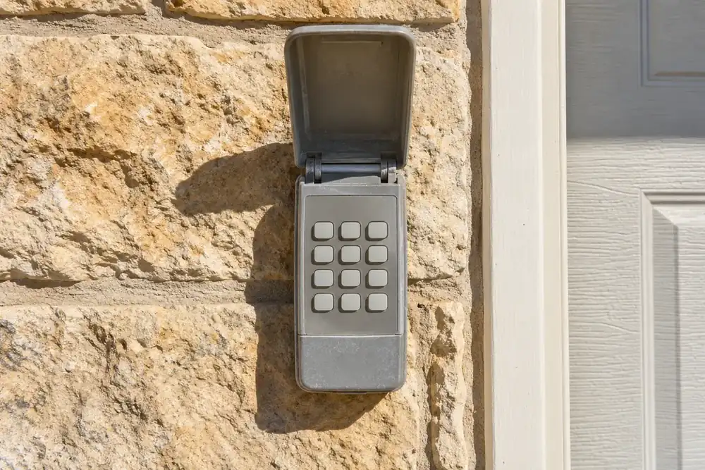 Sun-faded grey garage door keypad with a warped cover on a limestone wall
