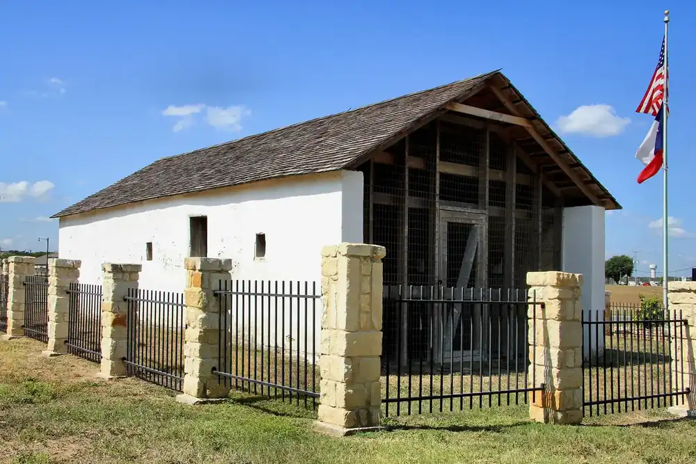 The whitewashed Harrison and Brown stagecoach stop behind a stone and iron fence in Selma, Texas